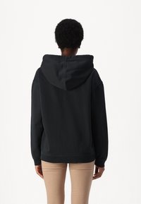 Zwarte hoodie met een relaxte fit, geribbelde manchetten en onderrand, en een zachte textuur. De achterkant toont een naadloos ontwerp van de capuchon.