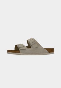 Μπεζ σανδάλι από σουέντ με δύο λουριά, ρυθμιζόμενες αγκράφες και πάτο από φελλό σε ανοιχτό γκρι φόντο.