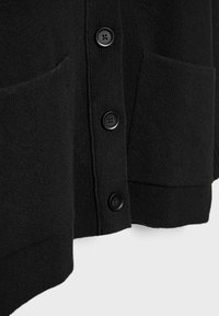 Gros plan sur le devant d'un cardigan noir en tricot montrant trois boutons noirs et deux poches plaquées à l'avant.