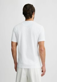 Hvid bomulds T-shirt med korte ærmer, rund hals og en glat tekstur; har diskret syning omkring halsudskæringen.