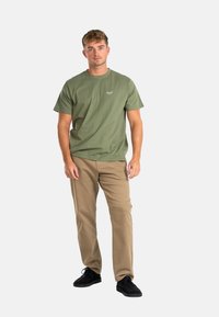 Olive green cotton t-shirt with short sleeves and a logo on the chest, paired with light beige pants and black shoes. Simple, casual outfit.
