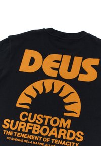 Black cotton t-shirt featuring bold orange text. Design includes a sun graphic and branding: "DEUS CUSTOM SURFBOARDS" with additional details below.