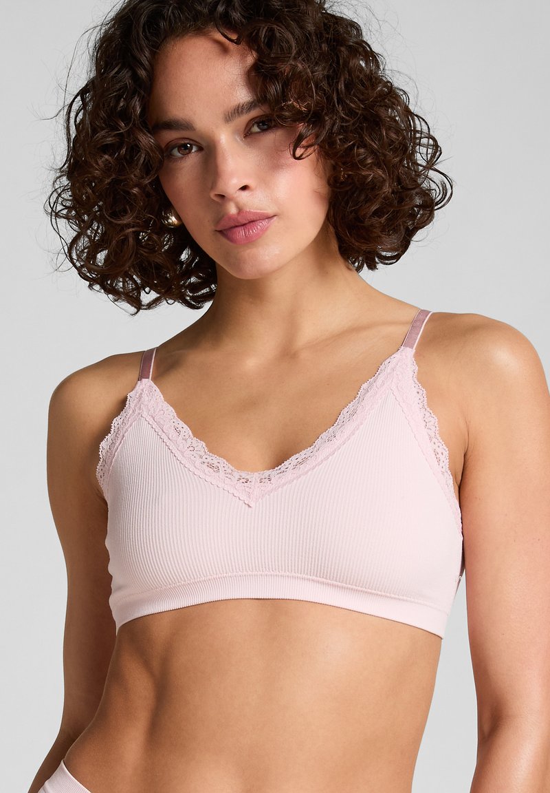 Lichtroze geribbelde bralette met een V-halslijn met kantafwerking en verstelbare bandjes. Zachte stof met een gladde textuur.