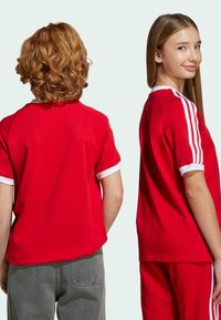 Röda t-shirtar med vita detaljer och ribbade ärmslut, med korta ärmar och lös passform, visas på två modeller från bak- och sidoräna.