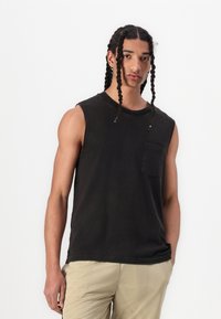 T-shirt sans manches noir en coton, avec un col rond et une poche avant, associé à un short texturé beige clair.
