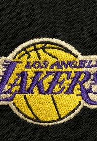 Schwarzer Stoff mit einem gestickten Logo der Los Angeles Lakers, das einen gelben Basketball und lila Text zeigt.