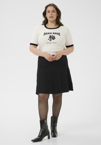 Top blanco de manga corta con ribete negro y texto gráfico, combinado con una falda negra acampanada y botas negras de tobillo con punta. 