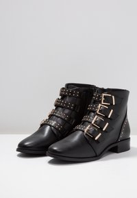 Bottines en cuir noir avec quatre sangles ajustables ornées de boucles en or, des accents cloutés, un bout pointu et un petit talon carré.