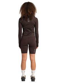 Brun atletisk långärmad topp och shorts, med en slank design och "ATW"-logotypdetaljer. Materialet verkar sträckt och mjukt.