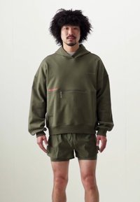 Olivengrøn hoodie med en frontlomme med lynlås og ribbede ærmer, parret med matchende shorts. Stoffet er blødt med en let glans.
