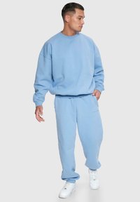 Hellblaues Sweatshirt und passende Jogginghose aus weichem Material, mit lockerer Passform und elastischen Bündchen. Weiße Sneakers vervollständigen das Outfit.