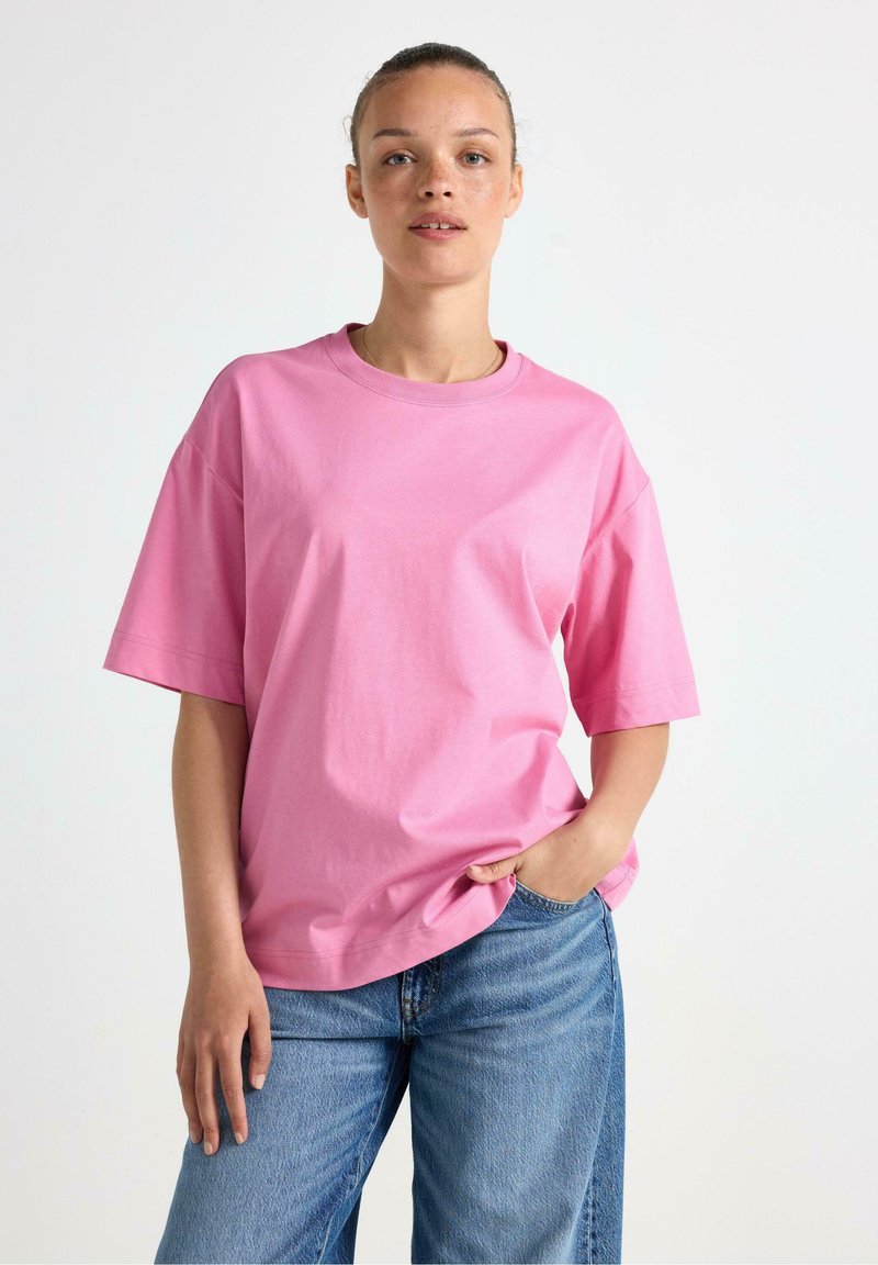 Lyserød bomulds t-shirt med korte ærmer, rund hals og en afslappet pasform, parret med blå jeans, som har en blød tekstur og et enkelt design.