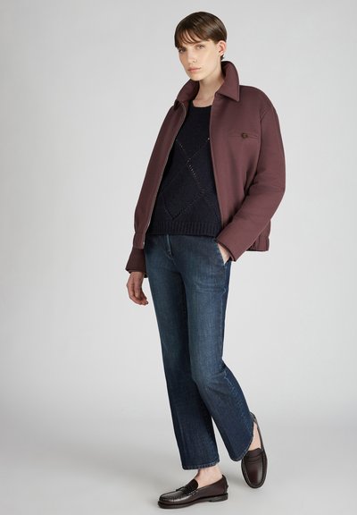 Bordeaux jasje met grote kraag, marineblauwe gebreide trui, slim-fit donkerdenim jeans en donkere instappers. Eenvoudig, strak design zonder patronen.