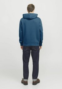 Felpa con cappuccio blu dal fit rilassato, superficie testurizzata e polsini a costine, abbinata a pantaloni in denim scuro e scarpe marroni.