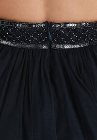 Svart tyllkjol med en strukturerad midja prydd med dekorativ silverpärlbeläggning och paljetter, samt dragkedja bak.