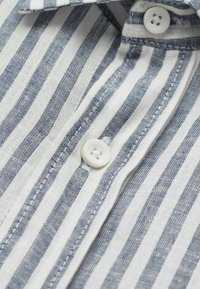 Gestreept shirt met afwisselend donkerblauwe en witte lijnen, gemaakt van een getextureerde stof, met een witte knoop en standaard kraagdetail.