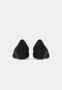 Scarpe nere a zeppa con una finitura liscia e opaca. Punta leggermente arrotondata, tacco basso e design minimalista senza hardware o dettagli visibili.