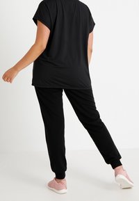 Top negro de mangas cortas y pantalones jogger negros, ambos hechos de una tela suave, combinados con zapatillas de deporte rosa claro. Diseño simple y casual.