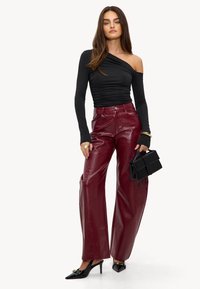 Zwarte one-shoulder top met ruching, gecombineerd met bordeauxkleurige faux leren brede broek met een gestructureerde afwerking. Zwarte handtas en spitse hakken.