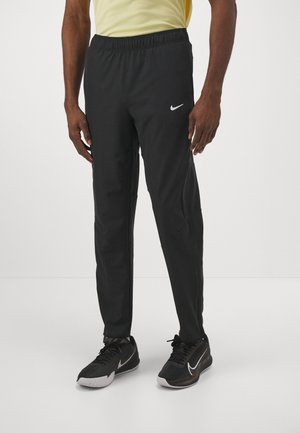Sorte Nike træningsbukser med elastisk talje, tætsiddende design og sidelommer. Bæres med sorte træningssko med hvide detaljer.