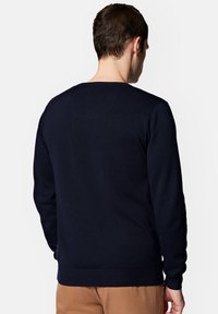 Granatowy sweter z dzianiny z okrągłym dekoltem, ribbowymi mankietami i dołem. Tkanina wydaje się miękka i teksturowana, idealna na codzienne stylizacje.