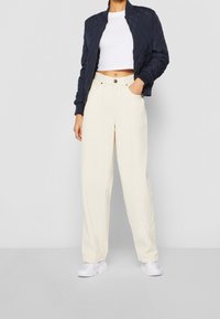 Giacca bomber imbottita navy, t-shirt bianca corta e pantaloni larghi crema abbinati a sneaker bianche. Look semplice, moderno e informale.