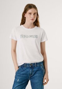 Balta medvilninė marškinė su šviesiai mėlyna "Pepe Jeans" grafika priekyje. Sukomplektuota su mėlynomis džinsinėmis kelnėmis, turinčiomis laisvą prigludimą ir nusidėvėjusią tekstūrą.