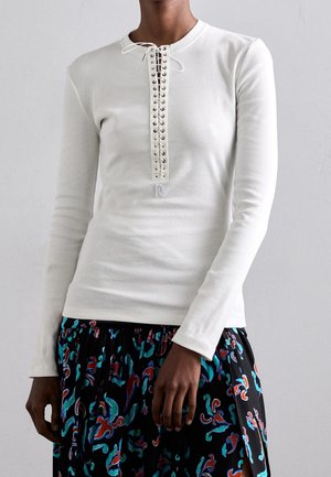 White ribbed long-sleeve shirt with a front lacing detail and eyelet accents. Paired with a black, patterned skirt featuring colorful abstract designs.