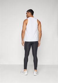 Top de tirantes blanco combinado con leggings negros. El top tiene un escote redondo y diseño sin mangas; los leggings son ajustados y de tela elástica. Zapatillas grises.
