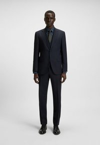 Marineblauw pak met een tailored fit, gestructureerde stof en een contrasterend blauw patroon overhemd. Inclusief een stropdas en zwarte leren schoenen.