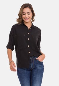 Zwarte button-up shirt gemaakt van textuurstof, met twee borstzakken en opgerolde mouwen. Gepaard met blauwe jeans.