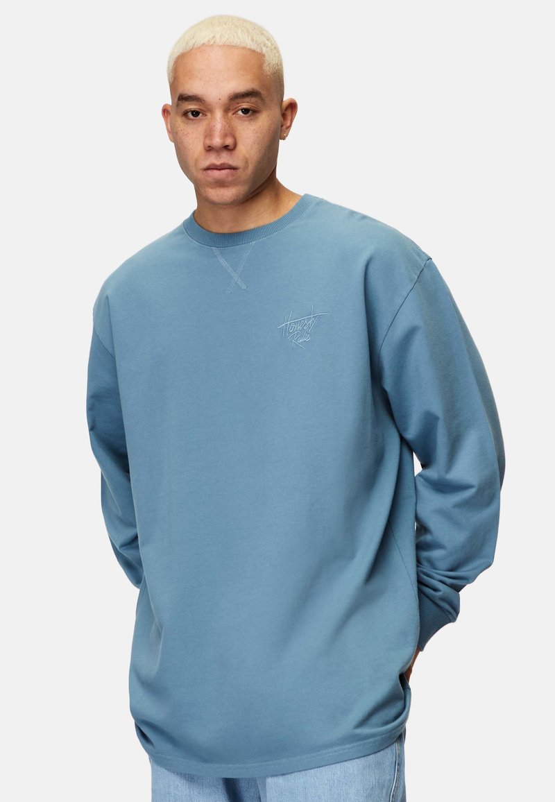 Blå sweatshirt i mjukt tyg, med rund halsringning och långa ärmar. Inkluderar en diskret logotyp på vänster bröst och ribbade muddar.