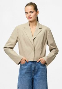 Beskåret beige blazer med hakkede revers, enkelt knaplukning og lange ærmer, kombineret med højttaljede blå denimjeans.