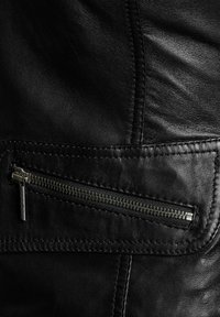 Crna kožna jakna s patentnim zatvaračem i metalnom opremom, detaljima šivanja i glatkom teksturom. Klasični dizajnerski elementi su prisutni.