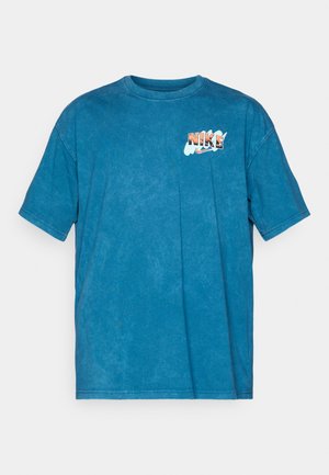 Camiseta de algodón azul con mangas cortas, cuello redondo y una textura desgastada. Presenta un logo de "NIKE" multicolor en el pecho.