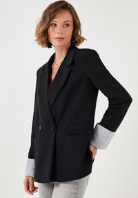Černý dvouřadý blazer s přiléhavým střihem, se šedými texturovanými manžetami, strukturovanými klopami a postranními kapsami.