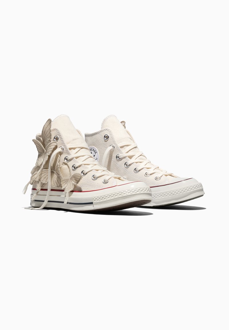 Elfenbeinfarbene High-Top-Sneaker aus Canvas mit Gummisohlen, mit Schmetterlingsverzierungen an den Seiten und weißen Schnürsenkeln.