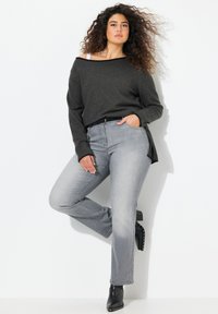 Maglione grigio a spalle scoperte abbinato a jeans grigi chiari a gamba dritta, completato da stivali neri alla caviglia con accenti borchiati.