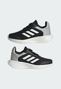 Scarpe da ginnastica nere e grigie con tomaia in mesh, caratterizzate da tre strisce bianche, una suola in gomma e un collare imbottito per il comfort.