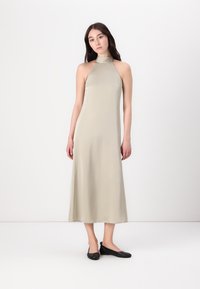 Vestito beige con scollo all'americana realizzato in tessuto liscio, con una forma A-line fluida e cuciture minime. La modella indossa delle ballerine nere.