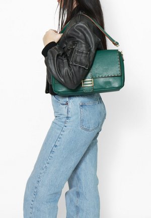 Groene handtas met textuur en een metalen sluiting, over de schouder gedragen. Vergezeld door een zwarte leren jas en lichtblauwe highwaisted jeans.