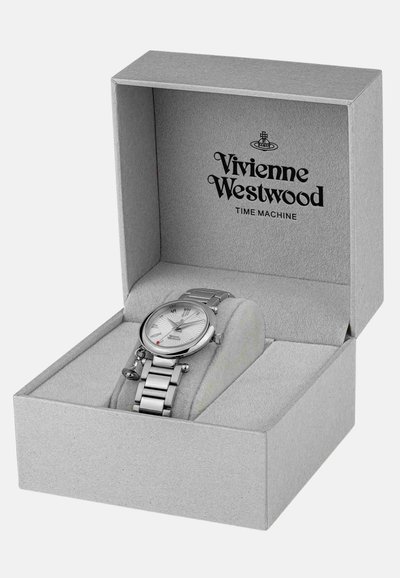 Montre en métal argentée présentée dans une boîte grise. La montre possède un cadran blanc texturé et un bracelet en acier inoxydable avec un accent rouge.