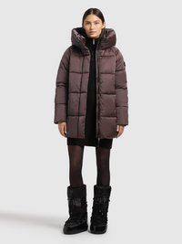 Brūna pūkaina jaka ar kapuci un izšūtu dizainu. Valkāta virs melnas adītas kleitas, kombinēta ar spīdīgām melnām sniega zābakām.