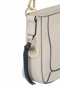 Beige Lederhandtasche mit goldenen Beschlägen, dunkelblauen Akzenten und einer runden Form. Verfügt über einen Logo-Anhänger und kontrastrierende Nähte.