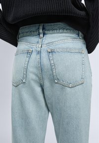 Jean en denim bleu clair taille haute avec poches arrière, porté avec un pull côtelé noir, vu de la taille vers le bas de dos.