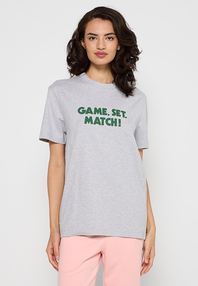 Graues Baumwoll-T-Shirt mit grünem Text, der "GAME, SET, MATCH!" in einer fetten, verspielten Schriftart zeigt. Kurzärmlig und mit einem lässigen Schnitt.
