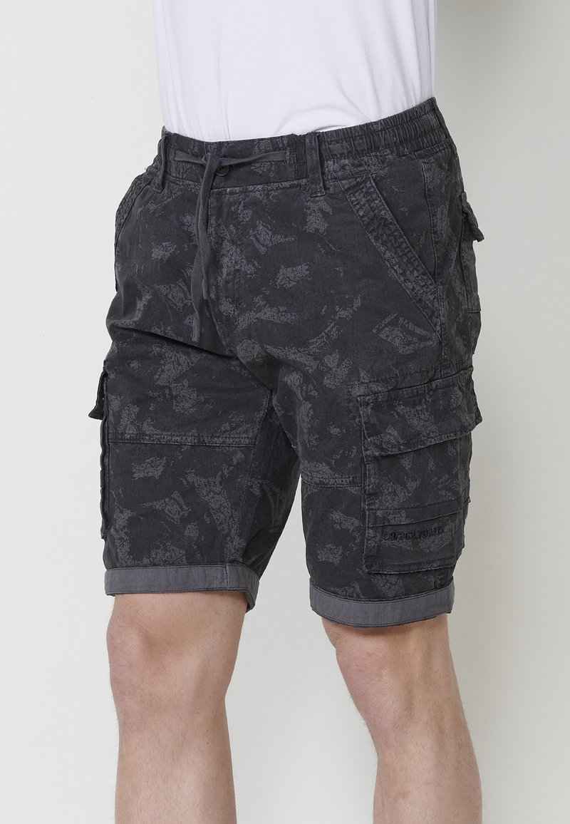 Shorts cargo gris foncé avec un motif subtil. Comprend plusieurs poches latérales, une taille avec cordon de serrage et des ourlets roulés.