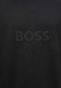 Μαύρο βαμβακερό T-shirt με ανάγλυφο, τονικό λογότυπο "BOSS" και περίπλοκα μοτίβα. Ο σχεδιασμός συνδυάζει την κομψότητα με μια μίνιμαλ αισθητική.