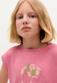 Roze t-shirt met korte mouwen met een bloemige schedelafbeelding in groen en roze. Zachte, gladde textuur en een ronde hals.
