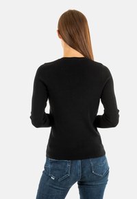 Un pull noir à manches longues avec un design ajusté, une texture côtelée et un col rond, porté avec un jean bleu visible à la taille.